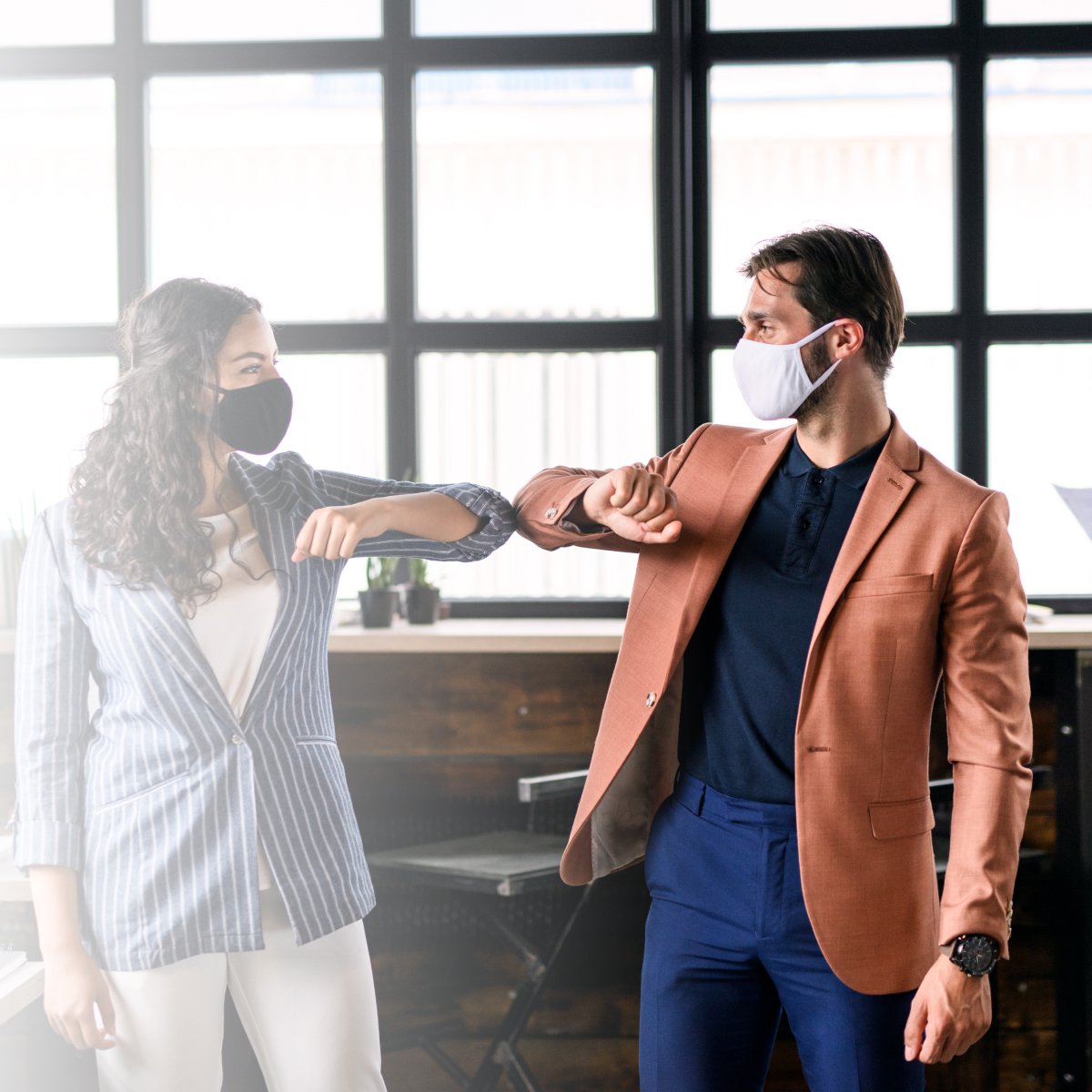 Young businesspeople with face masks working indoors in office, greeting.