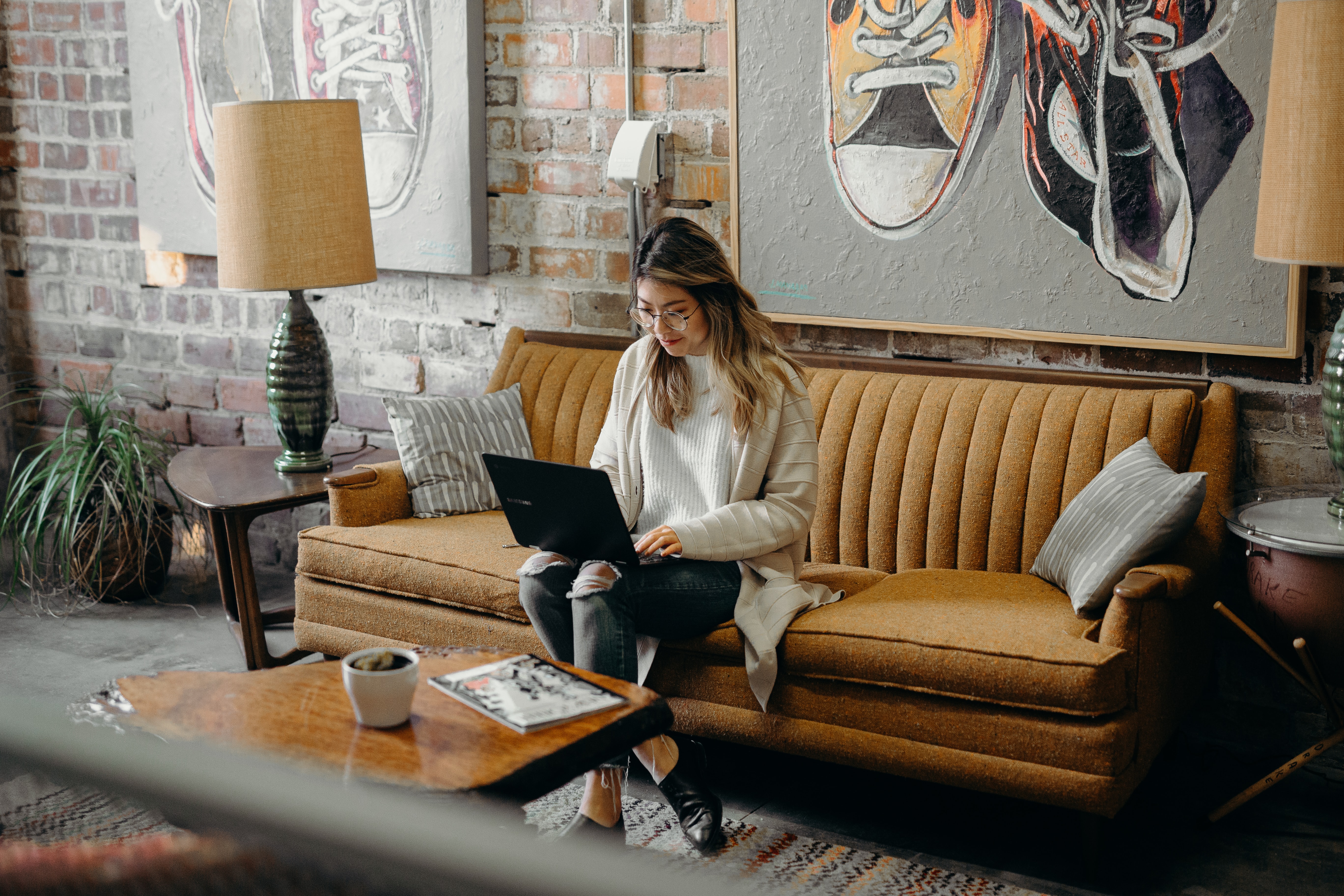 Woman working on laptop while sitting on home sofa.