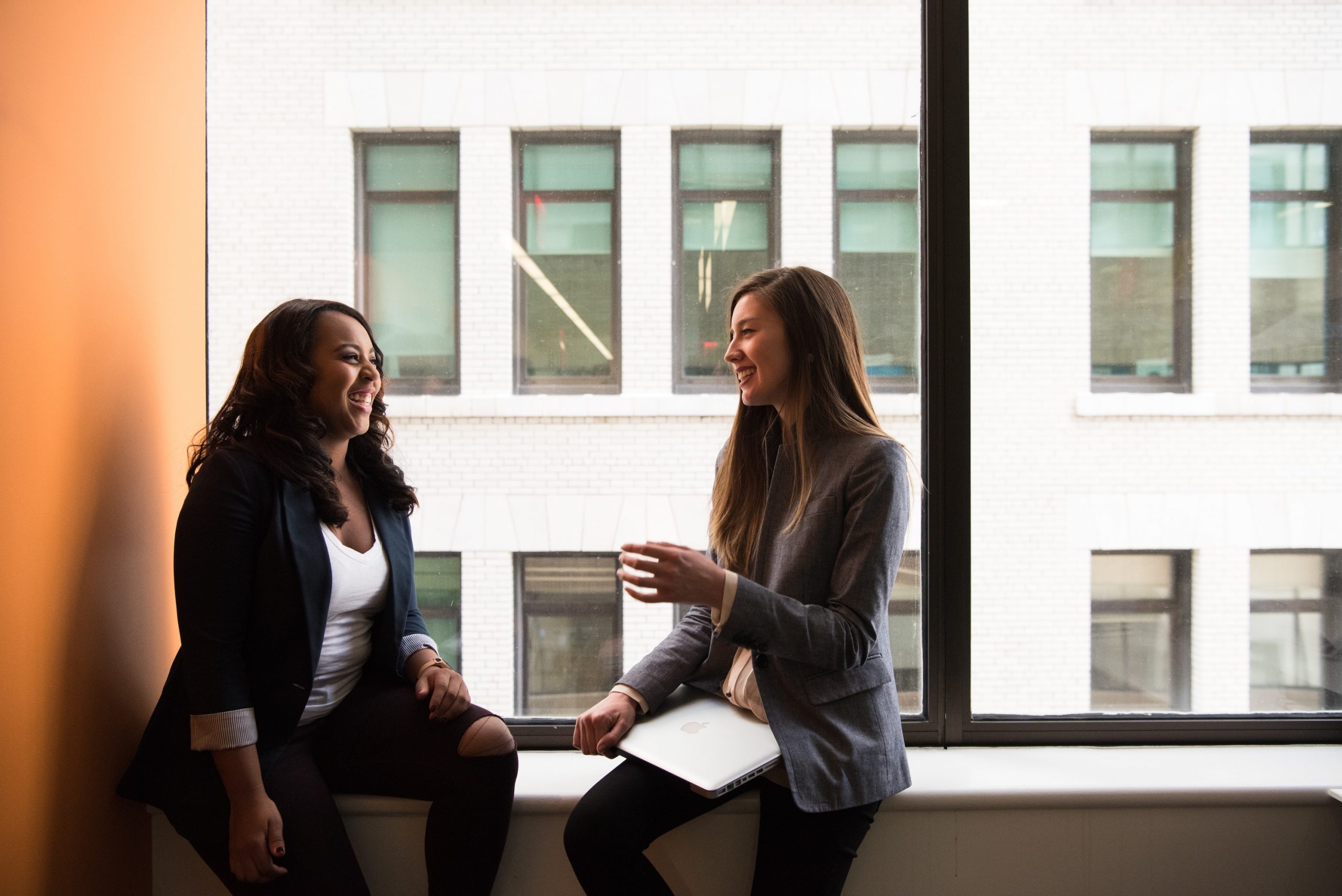 Two female employees having a conversation in front of a large window