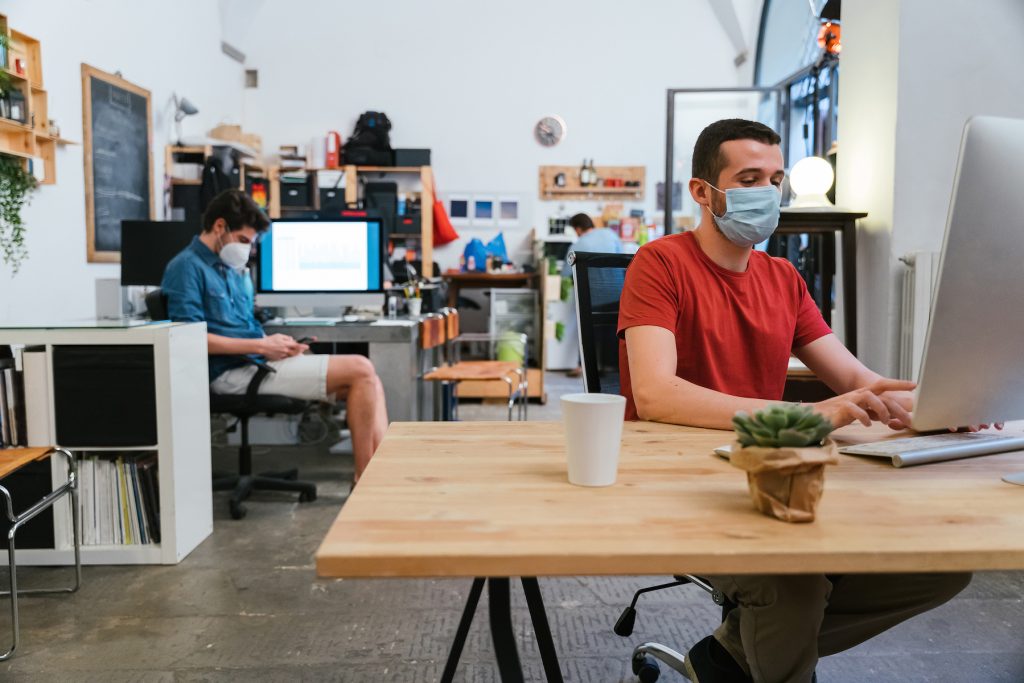 Millennials men with surgical mask at working at computer in office at distance for protection and prevention from Coronavirus, Covid-19