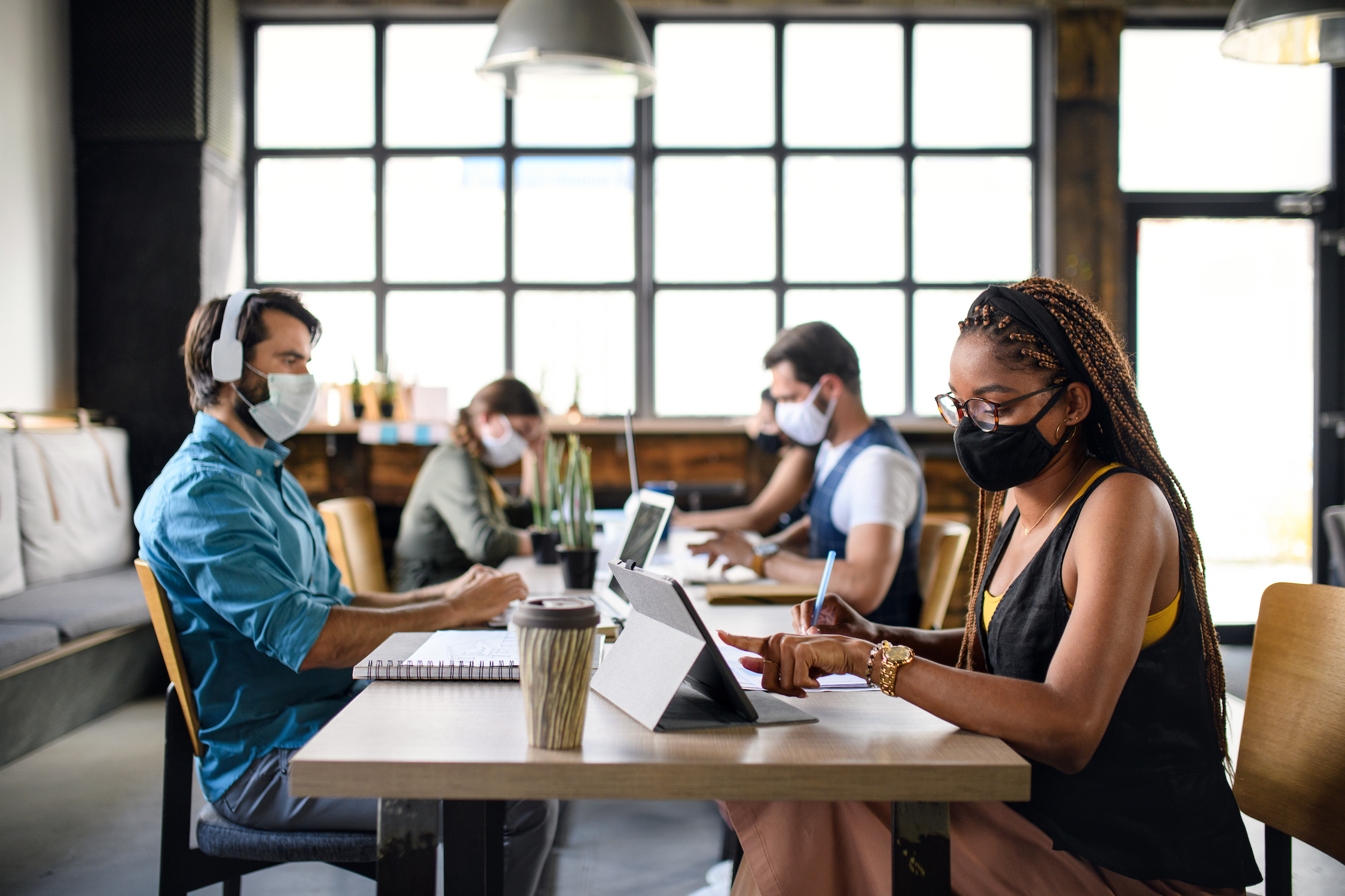 Business people with face masks working indoors in office, back to work after coronavirus lockdown.