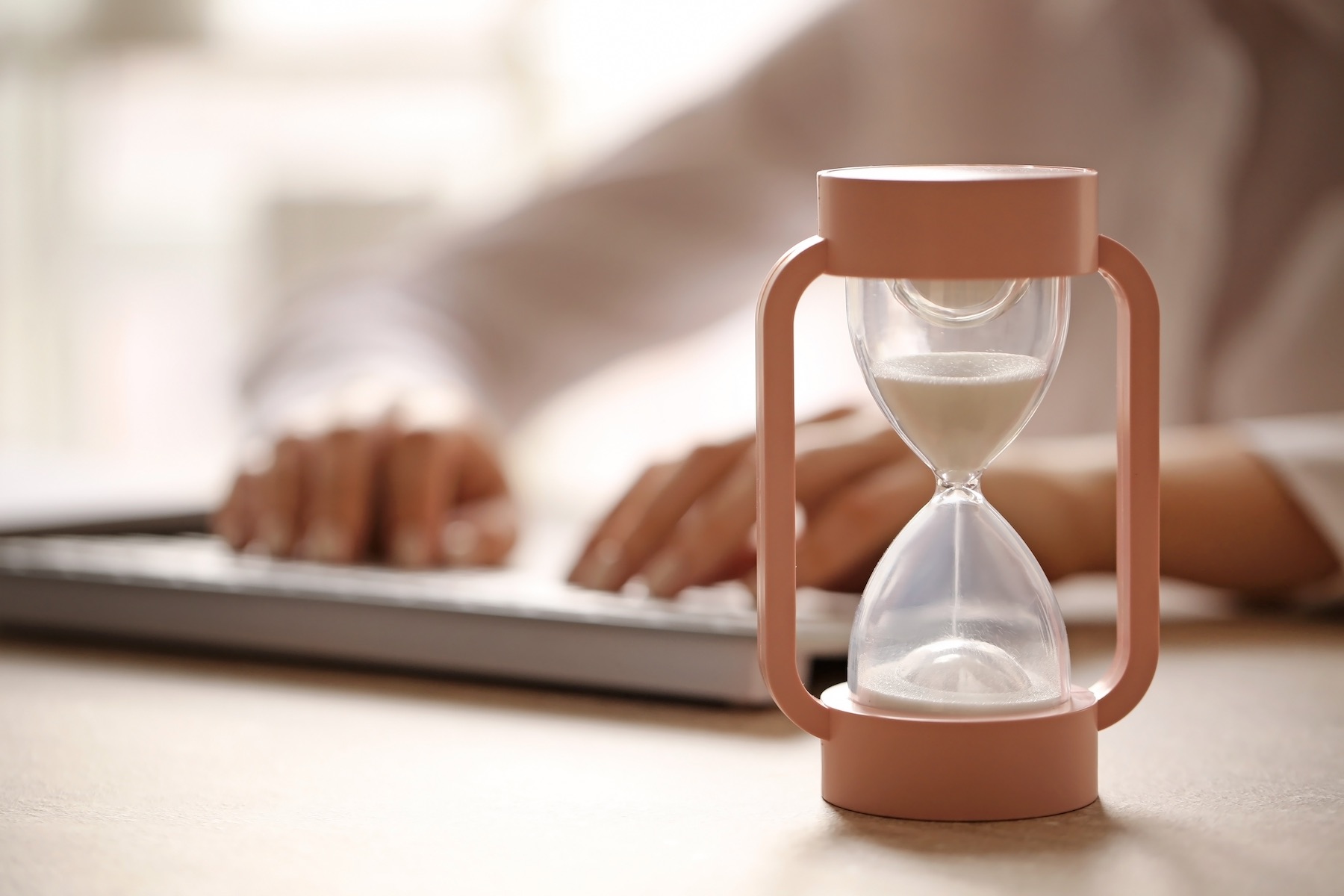 Hourglass and woman working on computer at table in office